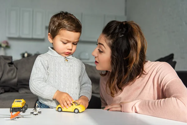 Вибірковий фокус жінки, що розмовляє з маленьким сином, граючи з іграшковими машинами вдома — стокове фото