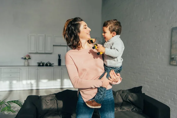 Щаслива жінка тримає маленького хлопчика з іграшковими машинами на руках вдома — стокове фото