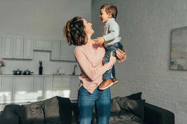 Sorrindo mulher segurando adorável pequeno filho a mãos em casa — Fotografia de Stock
