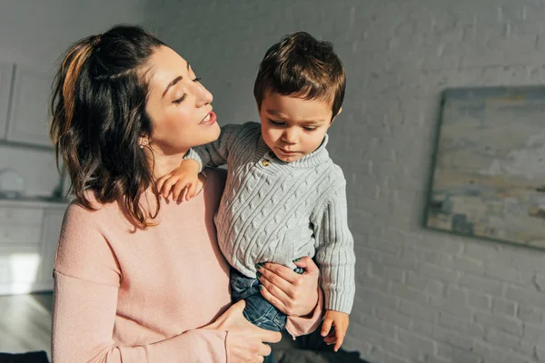 Madre hablando y sosteniendo adorable pequeño hijo en las manos en casa - foto de stock