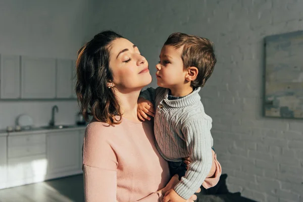 Ragazzo baci madre mentre lei tenendo lui su mani a casa — Foto stock
