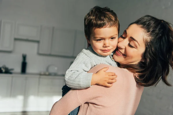 Nahaufnahme einer lächelnden Mutter, die zu Hause einen entzückenden kleinen Jungen auf Händen hält — Stockfoto