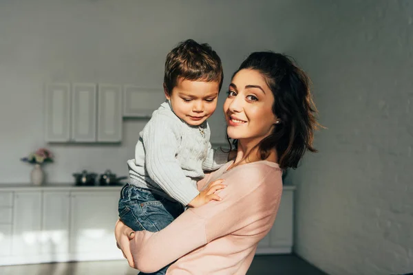 Mãe feliz segurando adorável pequeno filho a mãos em casa — Fotografia de Stock