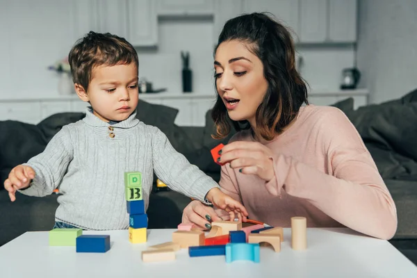 Adorable niño pequeño y su madre jugando bloques torre de madera juego en casa - foto de stock