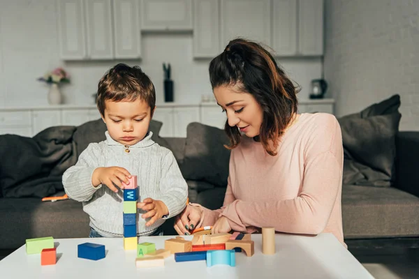 Focused little kid and his mother playing blocks wood tower game at home — Stock Photo