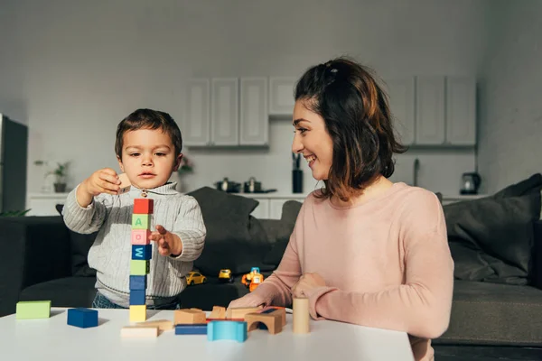 Enfoque selectivo de niño pequeño y su madre jugando bloques torre de madera juego en casa - foto de stock