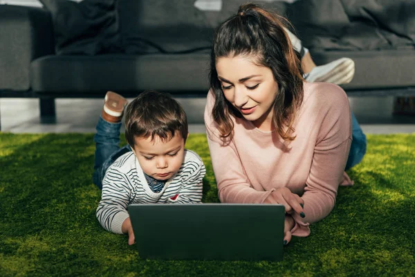 Mãe e pequeno filho deitado no chão com laptop em casa — Fotografia de Stock