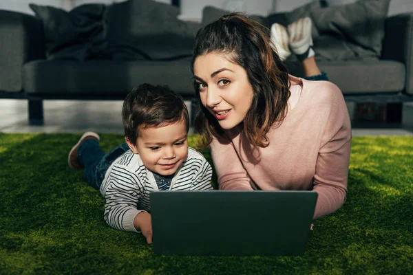 Schöne Frau und ihr Sohn auf dem Boden liegend mit Laptop zu Hause — Stockfoto