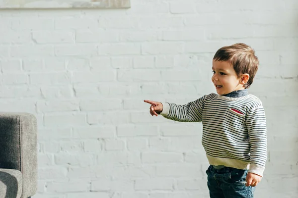 Niño sonriente señalando con el dedo en la sala de estar en casa — Stock Photo
