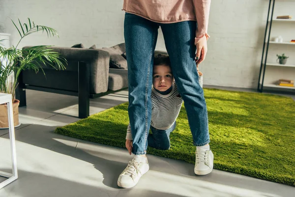 Niño pequeño sentado entre las piernas de la madre en la sala de estar en casa - foto de stock