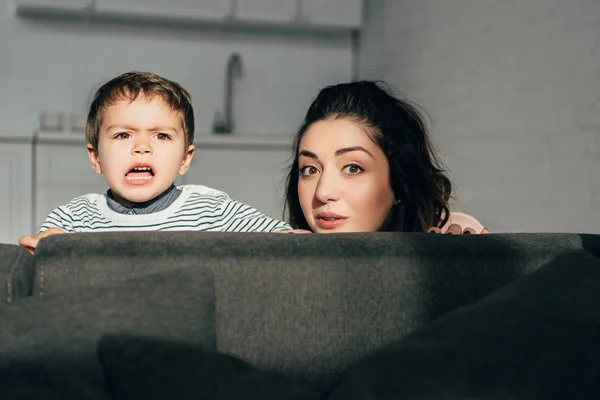 Hermosa madre y pequeño hijo emocional sentado en el sofá en casa - foto de stock