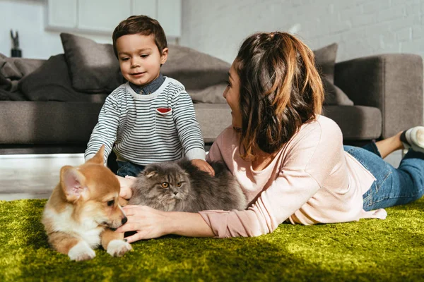 Madre e hijo tendidos en el suelo con perro y gato en la sala de estar en casa - foto de stock