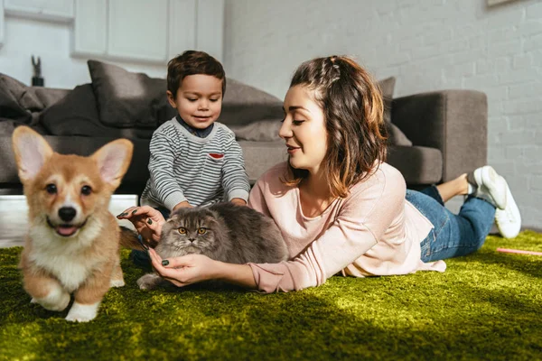 Mujer atractiva y niño pequeño acostado en el suelo con perro y gato en la sala de estar en casa - foto de stock