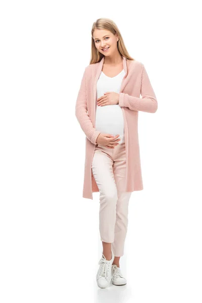 Longitud completa de la mujer embarazada en cárdigan rosa tocando el vientre aislado en blanco - foto de stock