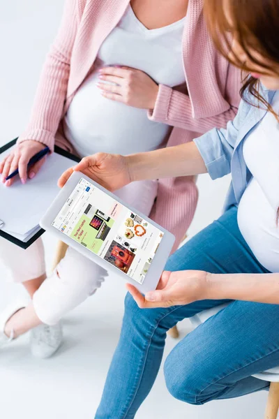 Vista recortada de mujeres embarazadas mirando tableta digital con la aplicación ebay en la pantalla durante la clase prenatal - foto de stock