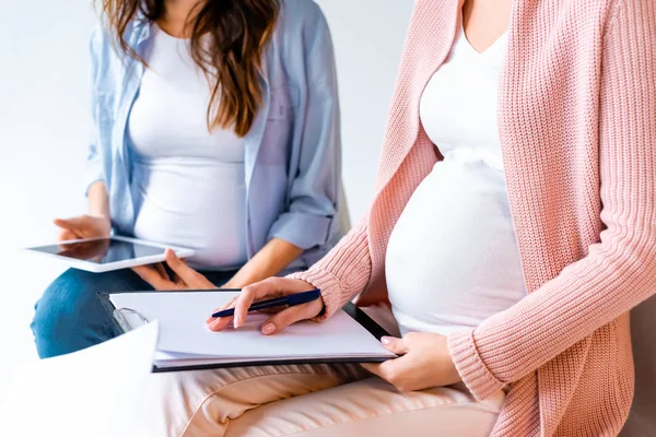 Mujeres embarazadas que usan tabletas digitales y escriben en formas durante la clase prenatal aisladas en gris - foto de stock