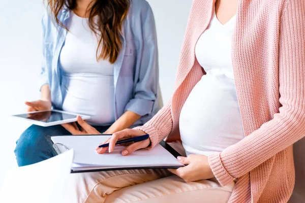 Gestantes em uso de tablet digital e escrita em formas durante a aula de pré-natal isoladas em cinza — Fotografia de Stock