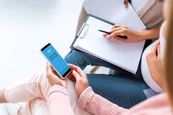 Vista recortada de mujeres embarazadas sosteniendo teléfono inteligente con aplicación de Skype en la pantalla - foto de stock