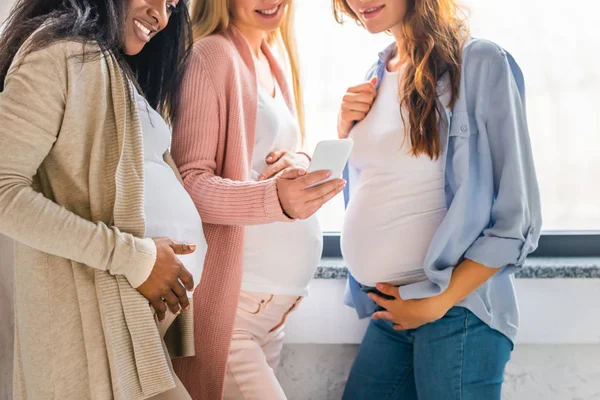 Многокультурные улыбающиеся беременные женщины с помощью смартфона — стоковое фото