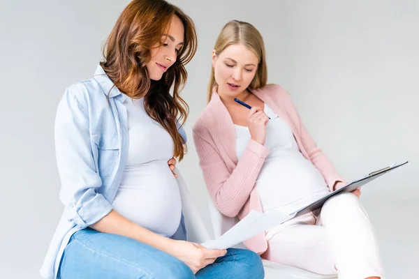 Mujeres embarazadas hablando durante la clase prenatal aisladas en gris - foto de stock