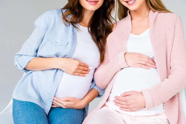 Обрізаний вид вагітних усміхнених жінок, що сидять на антенатальному класі ізольовані на сірому — стокове фото