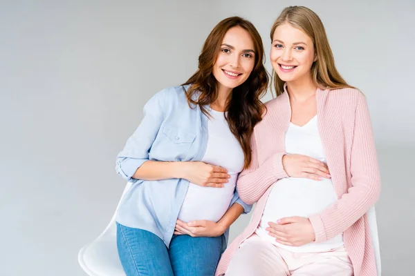 Embarazadas mujeres sonrientes sentadas en sillas aisladas en gris - foto de stock