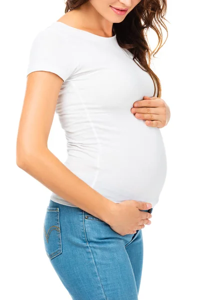 Vista recortada de la hermosa mujer embarazada tocando el vientre con ambas manos aisladas en blanco - foto de stock