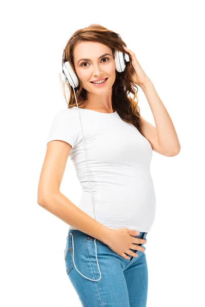 Mujer embarazada escuchando música y sosteniendo auriculares con la mano izquierda aislada en blanco - foto de stock