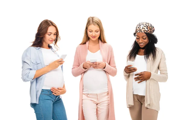 Hermosas mujeres embarazadas multiculturales utilizando teléfonos inteligentes aislados en blanco - foto de stock