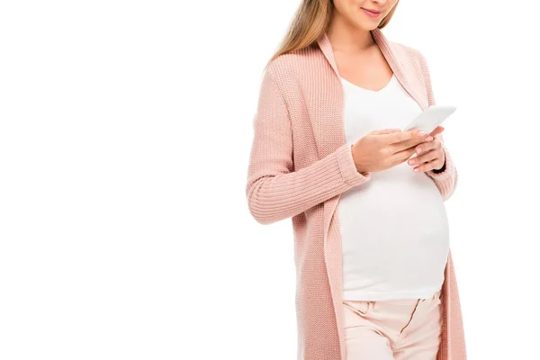 Vista recortada de la mujer embarazada en cárdigan rosa usando teléfono inteligente aislado en blanco - foto de stock