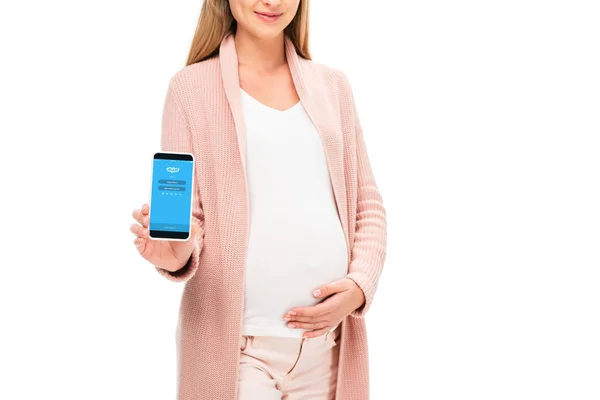Schöne lächelnde schwangere Frau hält Smartphone mit Skype-App auf dem Bildschirm isoliert auf weiß — Stockfoto
