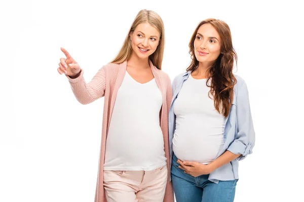 Mujeres embarazadas señalando algo con el dedo y mirando hacia otro lado aislado en blanco - foto de stock