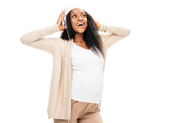 Mujer embarazada afroamericana extática escuchando música en auriculares aislados en blanco - foto de stock