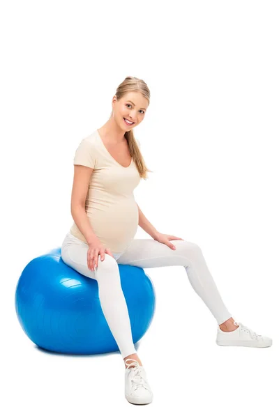 Donna bionda incinta seduta sulla palla fitness e che tiene le mani sulle ginocchia isolate su bianco — Foto stock