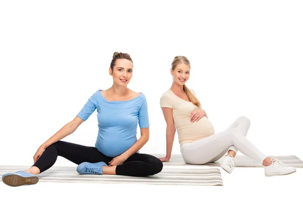 Two pregnant women sitting on fitness mats isolated on white — Stock Photo