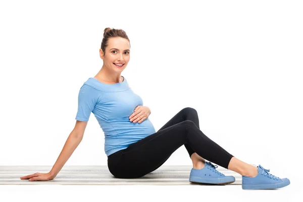 Grávida de cabelos castanhos mulher sentada no chão com uma mão na barriga isolada no branco — Fotografia de Stock