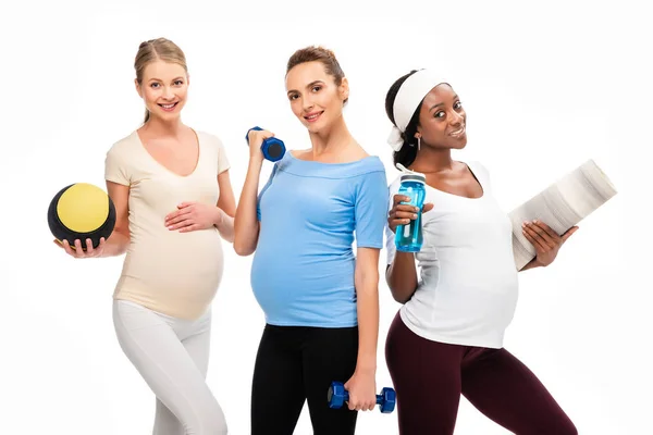 Три усміхнені вагітні жінки тримають гантелі та фітнес речі ізольовані на білому — стокове фото