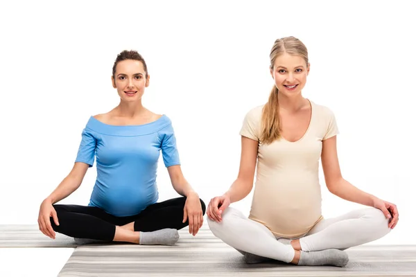 Two beautiful pregnant women sitting on floor and holding hands on knees isolated on white — Stock Photo