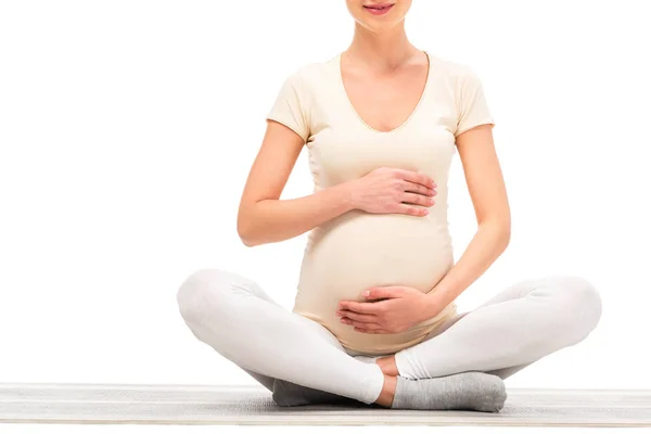 Visão cortada da mulher grávida sentada em postura de lótus e mantendo as mãos sobre a barriga isolada no branco — Fotografia de Stock