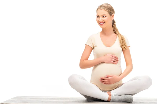Mujer embarazada sentada en pose de loto y mirando hacia otro lado aislada en blanco - foto de stock