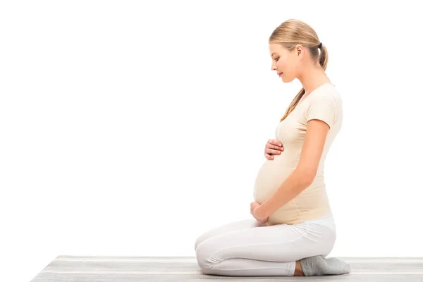 Mujer rubia embarazada sentada en el suelo en perfil aislado en blanco - foto de stock