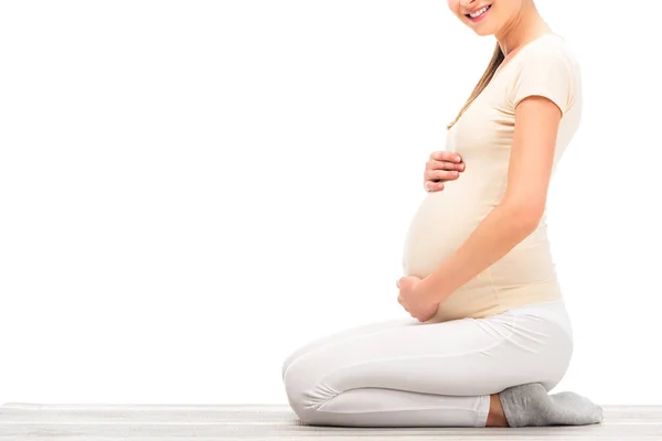 Обрізаний вид вагітної жінки, що сидить і тримає руки на животі ізольовано на білому — стокове фото