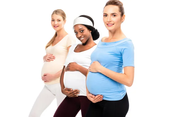 Drei schwangere Frauen, die Hände auf Bäuchen halten und isoliert auf weißem Grund lächeln — Stockfoto