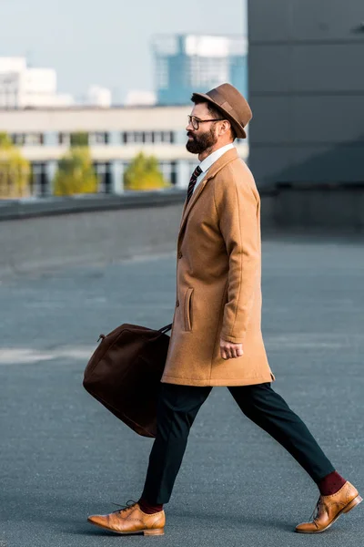 Vista lateral del hombre de negocios barbudo con bolsa caminando en el techo - foto de stock