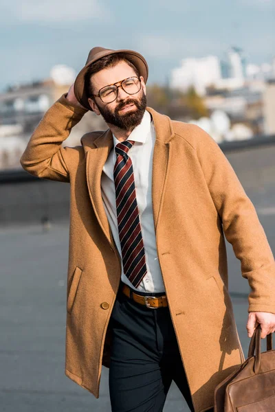Adult bearded businessman walking on roof and touching hat — Stock Photo