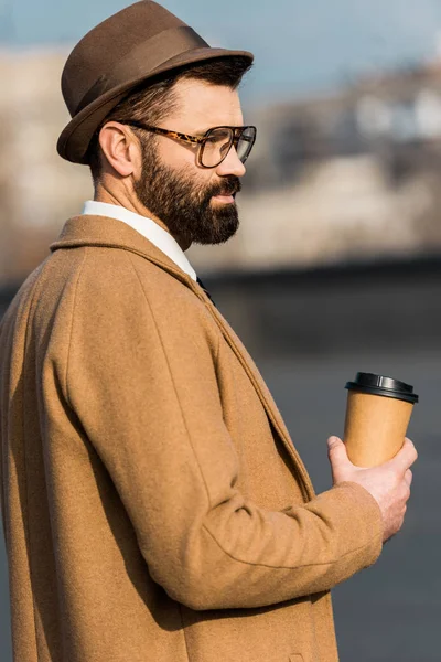 Взрослый красивый бизнесмен в шляпе держит кофе, чтобы пойти — стоковое фото