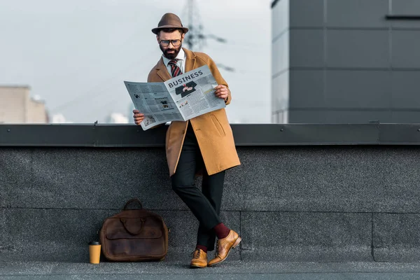 Adult bearded man standing with crossed legs and reading business newspaper on roof — Stock Photo