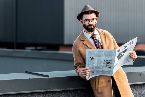 Handsome adult man in formalwear holding business newspaper and looking at camera — Stock Photo