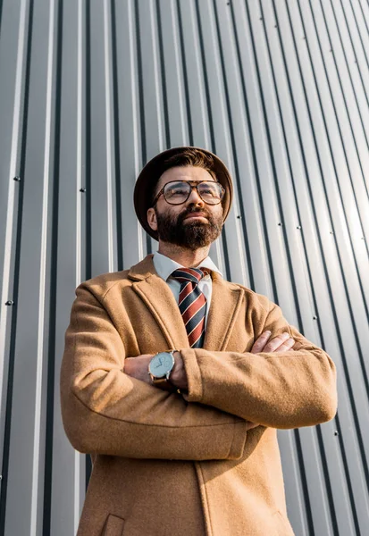 Vista de ángulo bajo del hombre de negocios en gafas de pie con los brazos cruzados - foto de stock