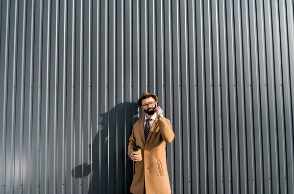 Bel homme d'affaires en manteau parlant sur smartphone et tenant du café à emporter — Photo de stock